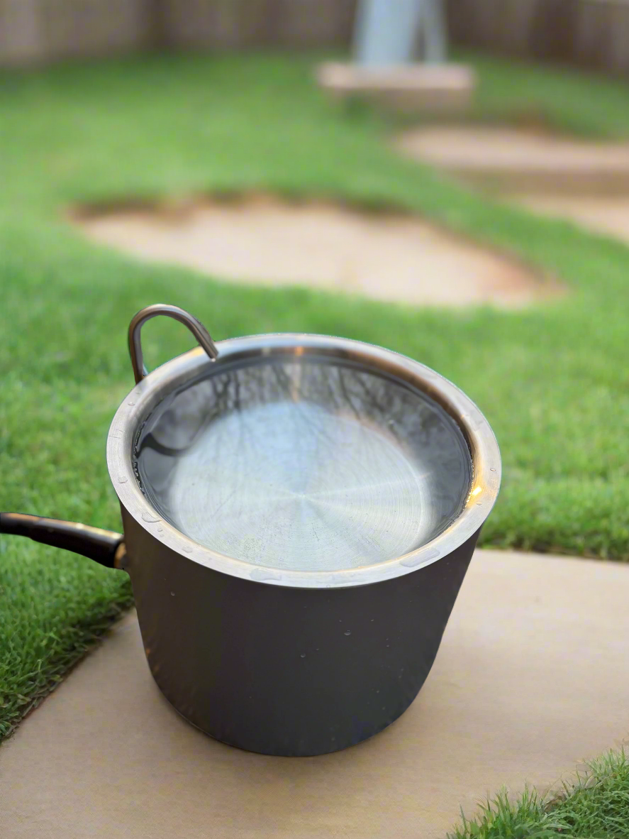 Black pot with water on a concrete surface with grass in the background